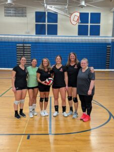 Women's volleyball team posing in gymnasium.